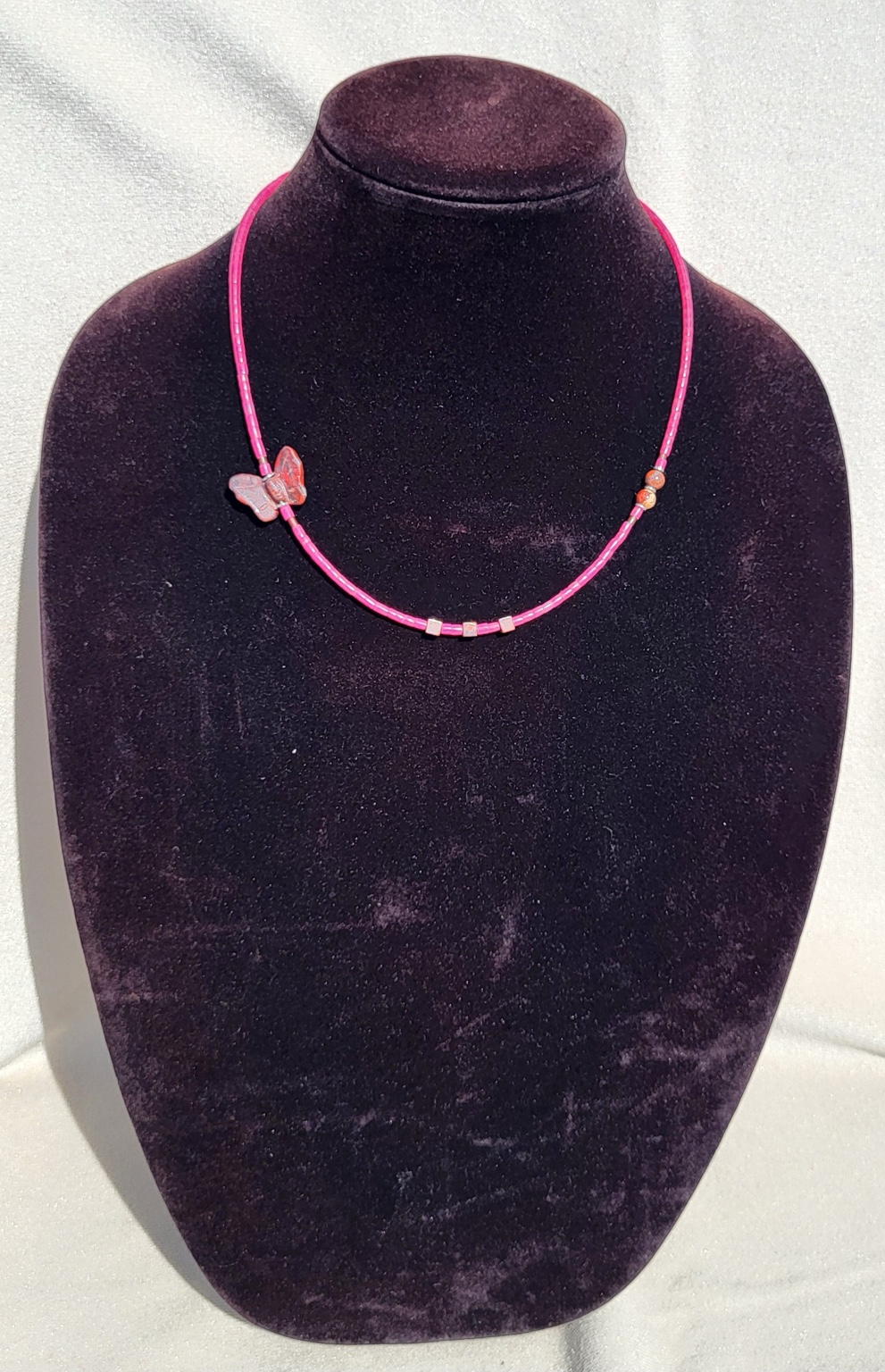 Hot pink beaded strand necklace with a carved stone butterfly at the side