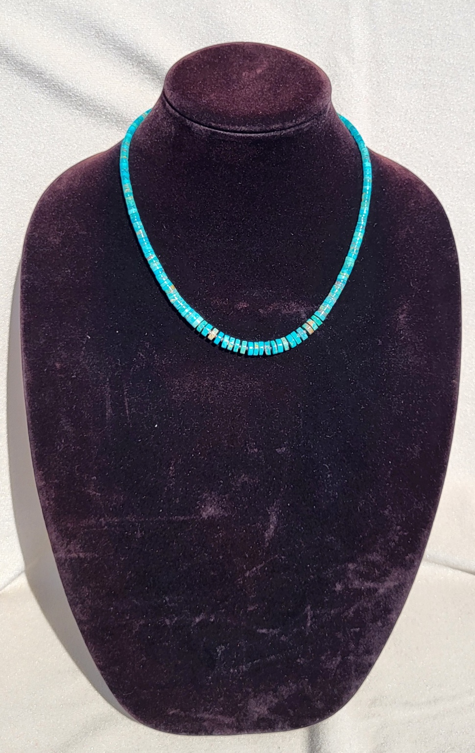 Graduated turquoise stone heishi necklace on a plum velvet display bust