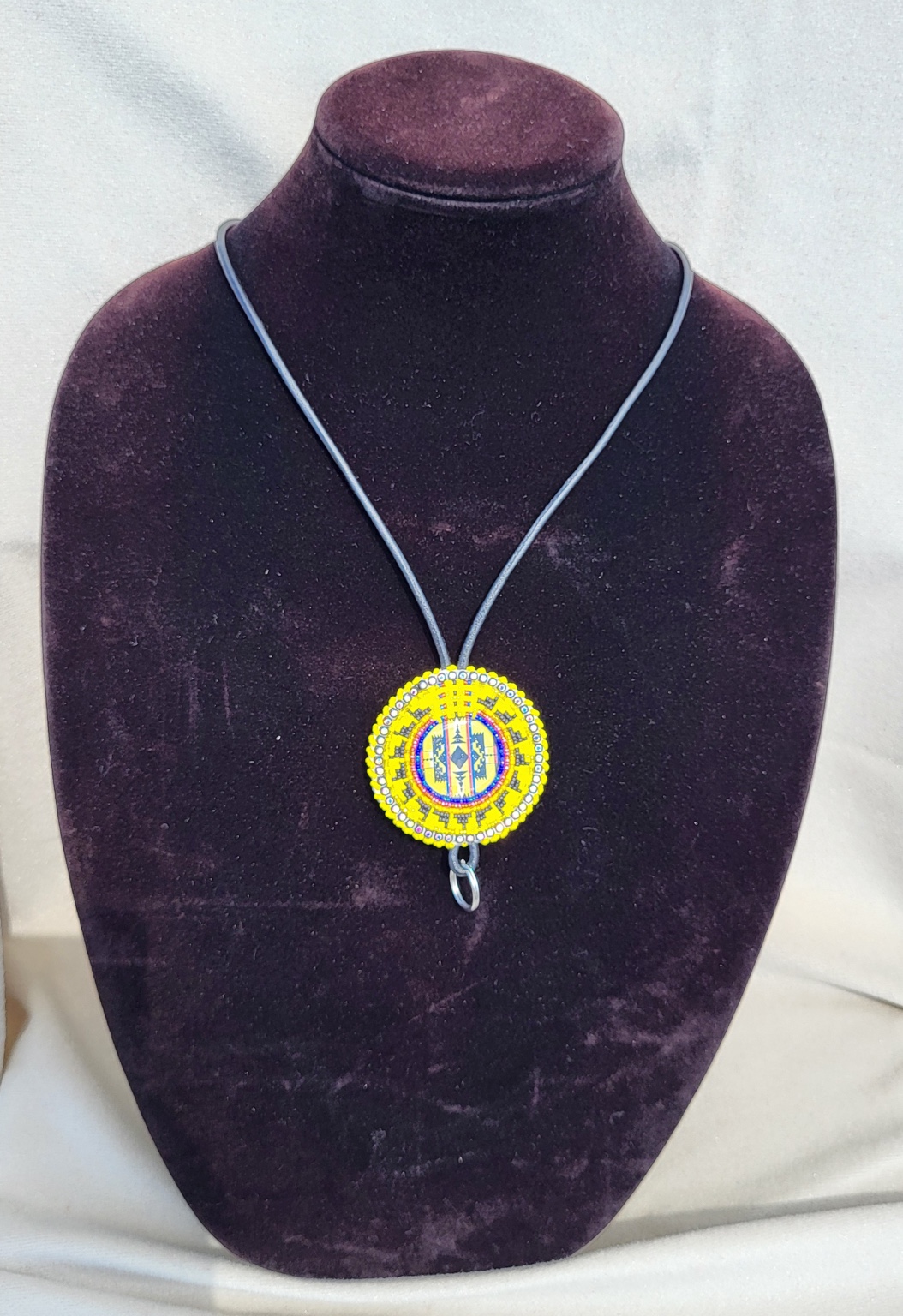 Round beaded medallion pendant in yellow, red, blue and white on a leather cord