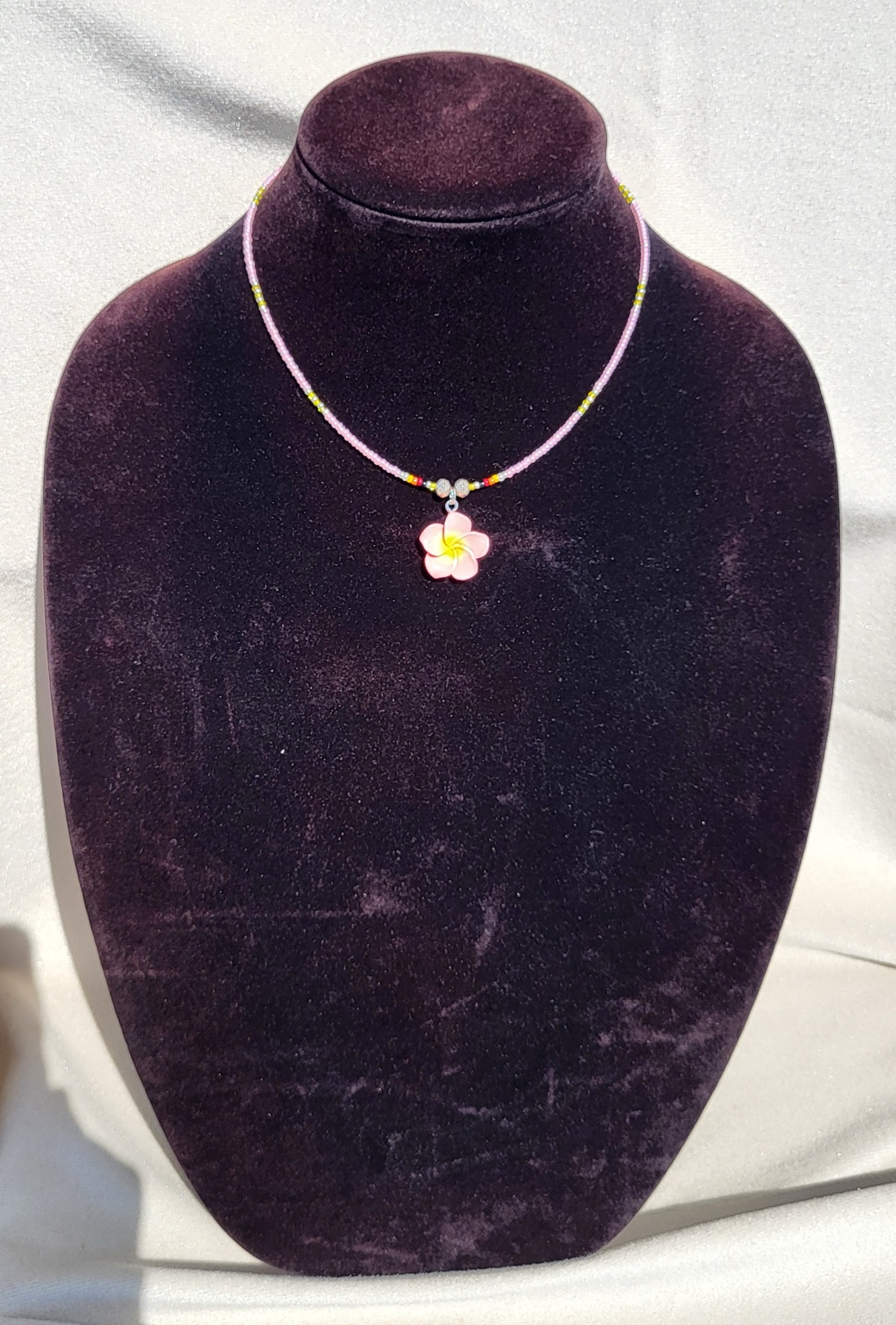 Pale pink seed bead necklace with a pink and yellow plumeria flower pendant