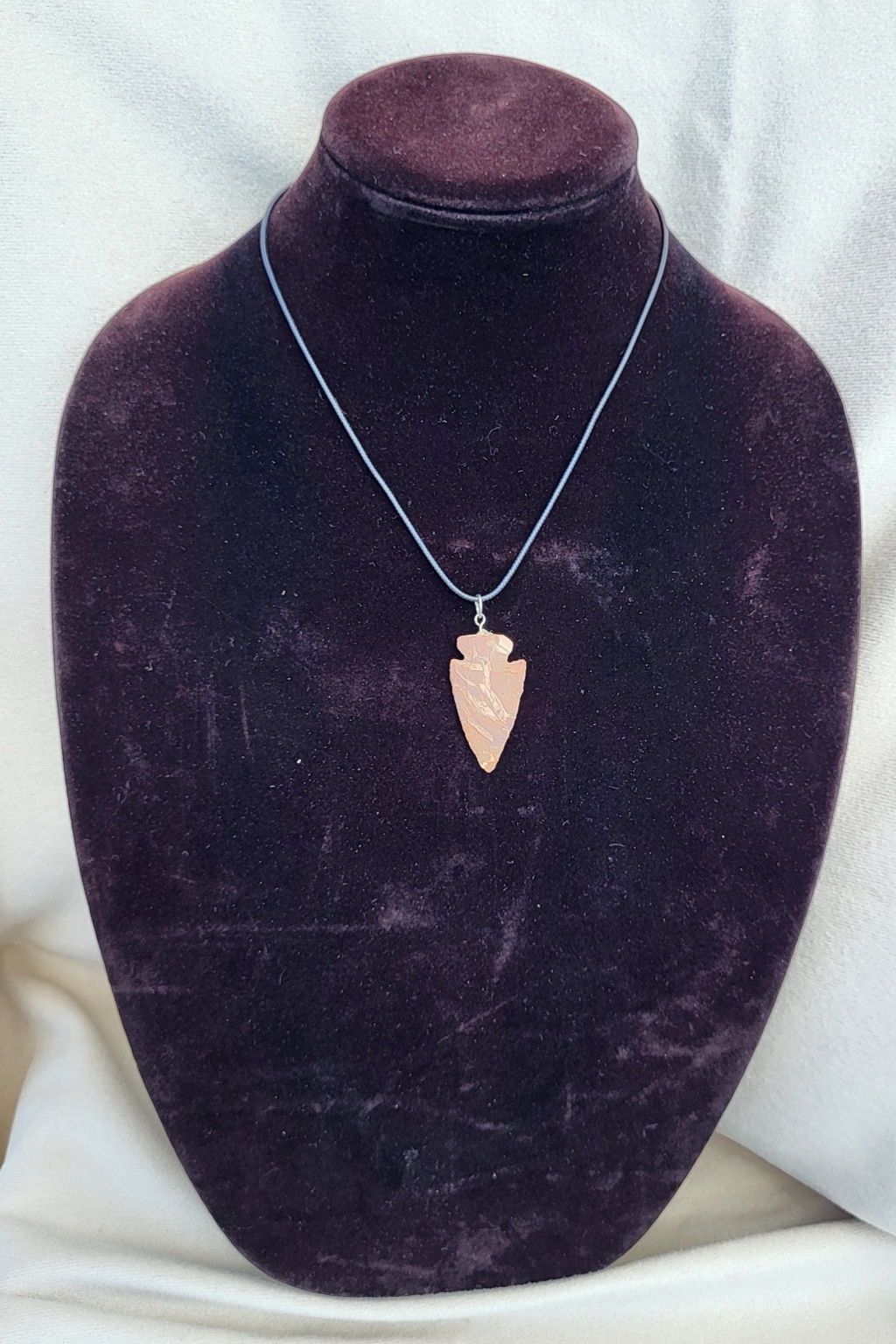 Banded rose-stone arrowhead pendant hung on a black cord necklace